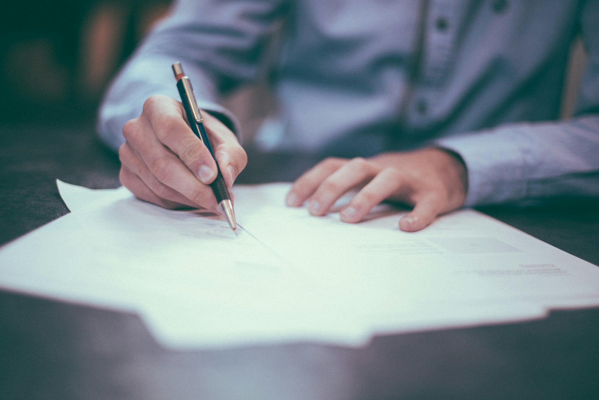 Hands reviewing paperwork with a pen at a desk.